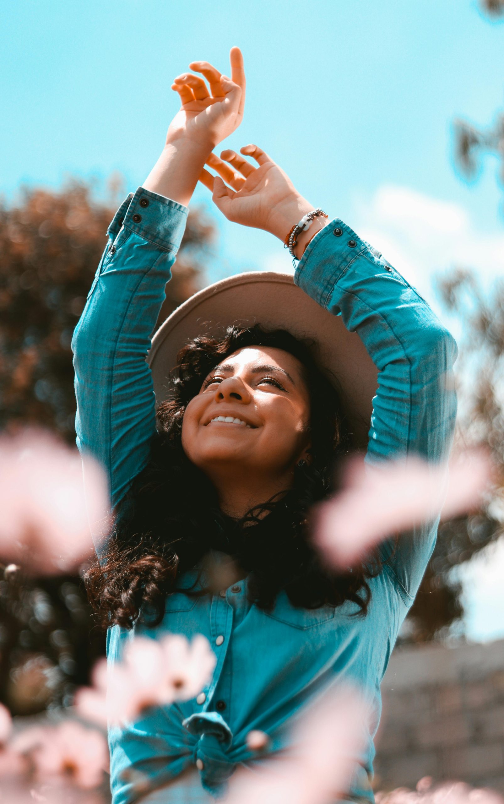 Woman with long hair and hat outdoors in spring, smiling and embracing nature.
